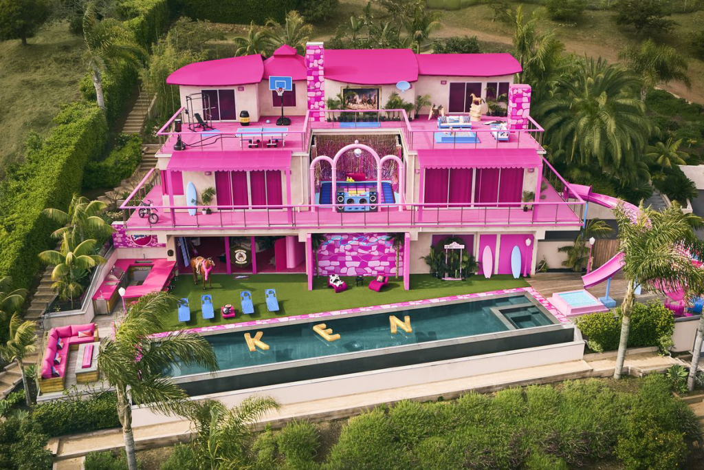 a pink house, on the California hills with a pool with floats spelling KEN in the pool.