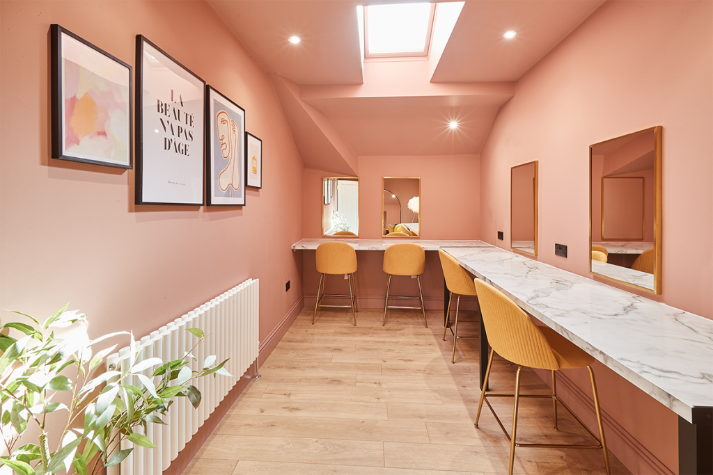 a peachy pink dressing room with a table and chairs in a L shape around the room
